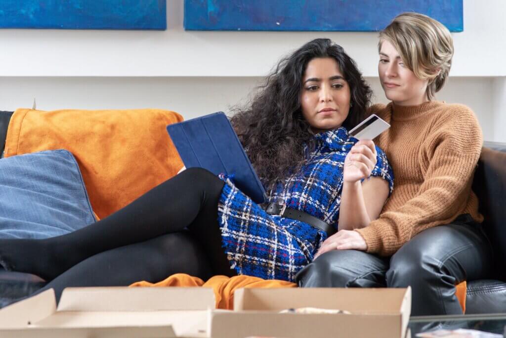 Two women sitting together closely on a couch looking at their credit card and financials