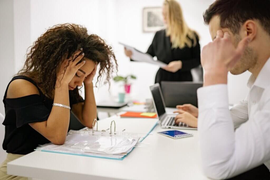A woman sits at a table and looks at a binder with her head in her heads in a stressed manner.